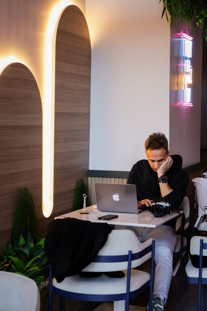 A young man focused on his laptop in a stylish cafe with modern lighting.